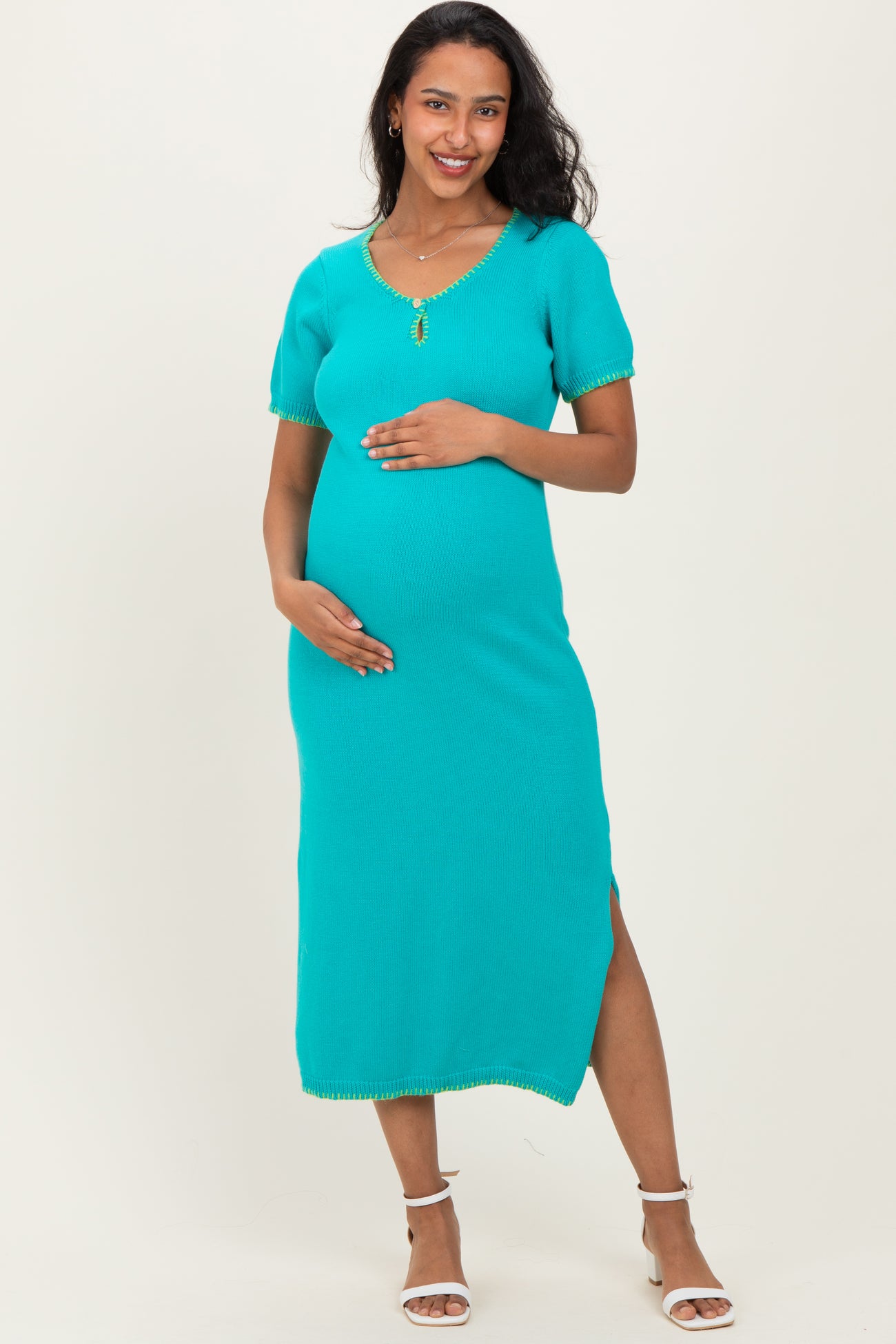 woman wearing a turquoise maternity knit dress with short sleeves and side slits, holding her baby bump