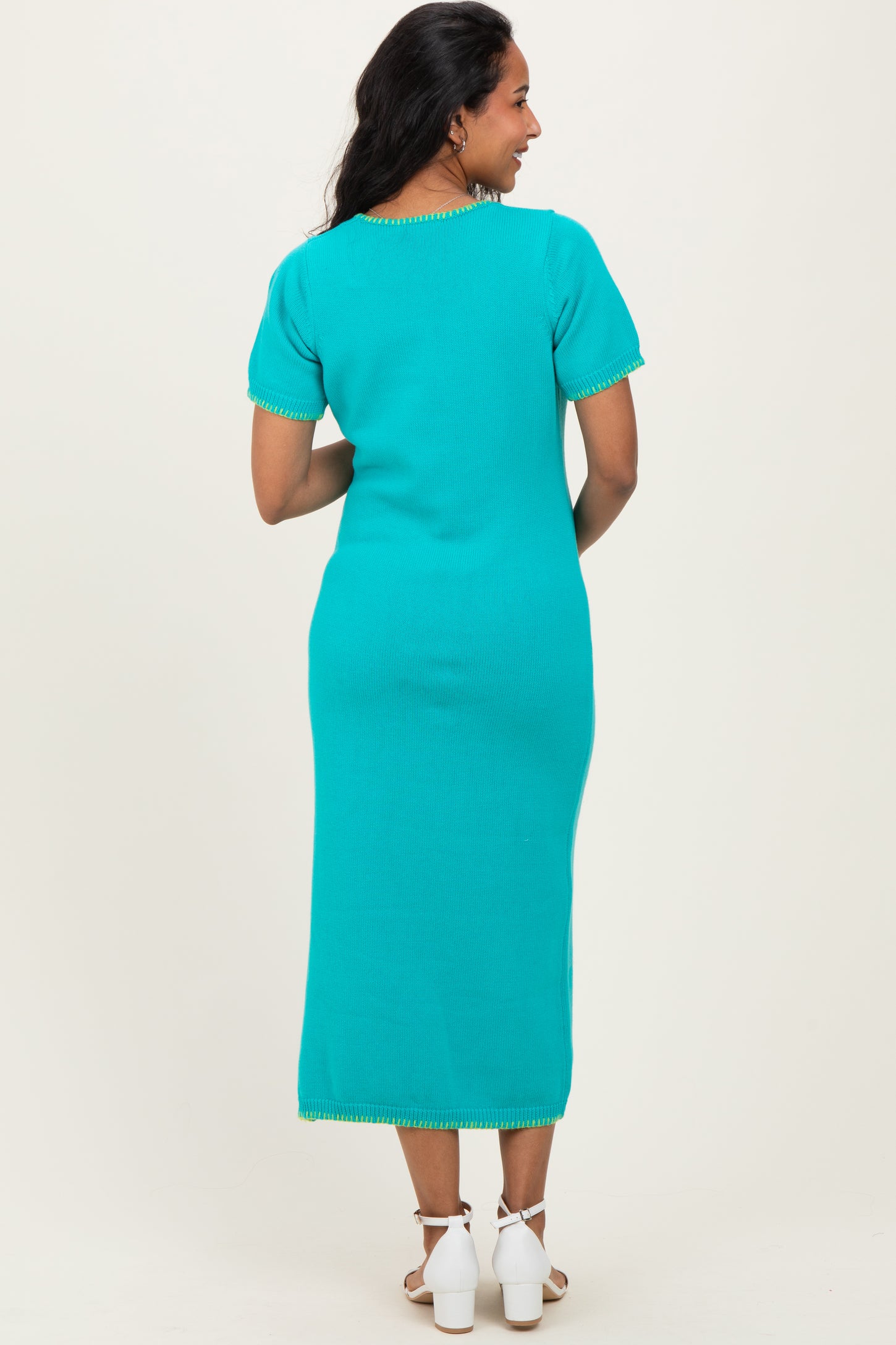 woman wearing a turquoise maternity dress with short sleeves and decorative hem details, showing a baby bump from the back