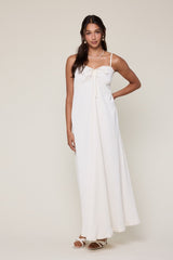 woman wearing a white maxi dress with bow detail and thin straps, standing casually with one hand on her hip