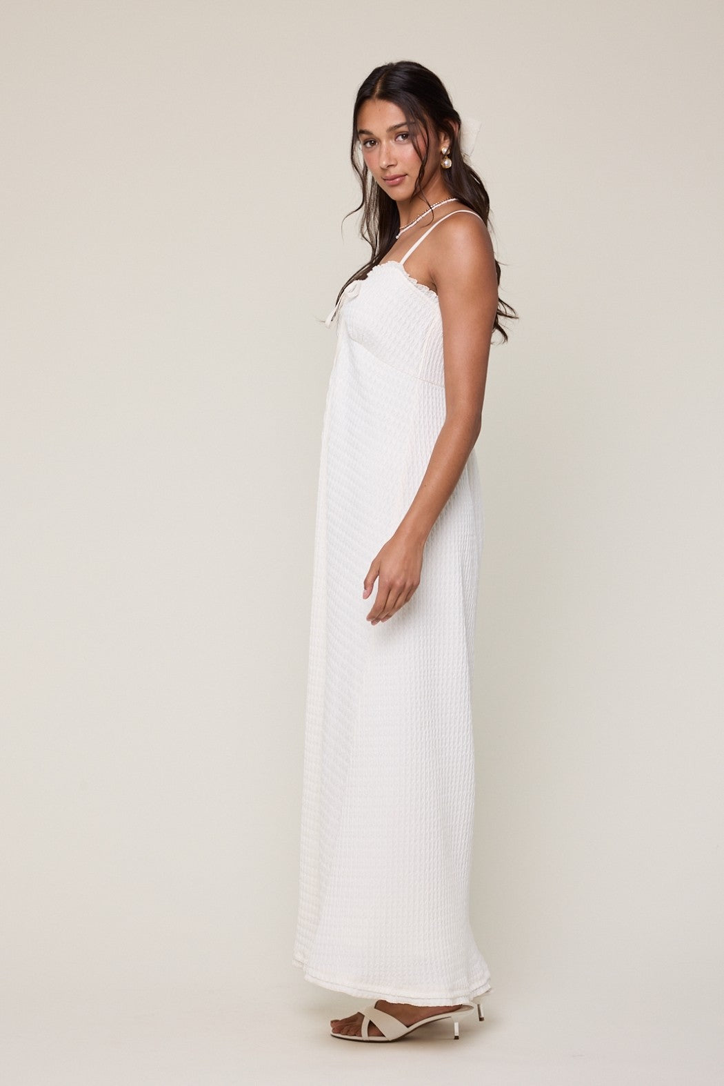 woman wearing a long white sleeveless maxi dress with a textured fabric and adjustable straps