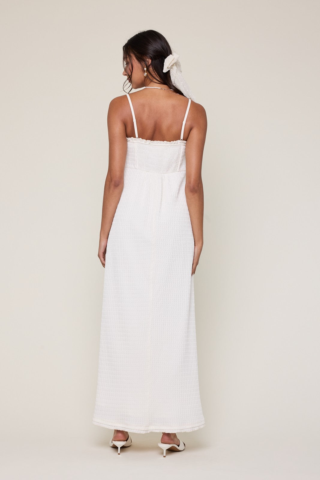 woman wearing a white long maxi dress with thin straps and a textured finish, seen from the back