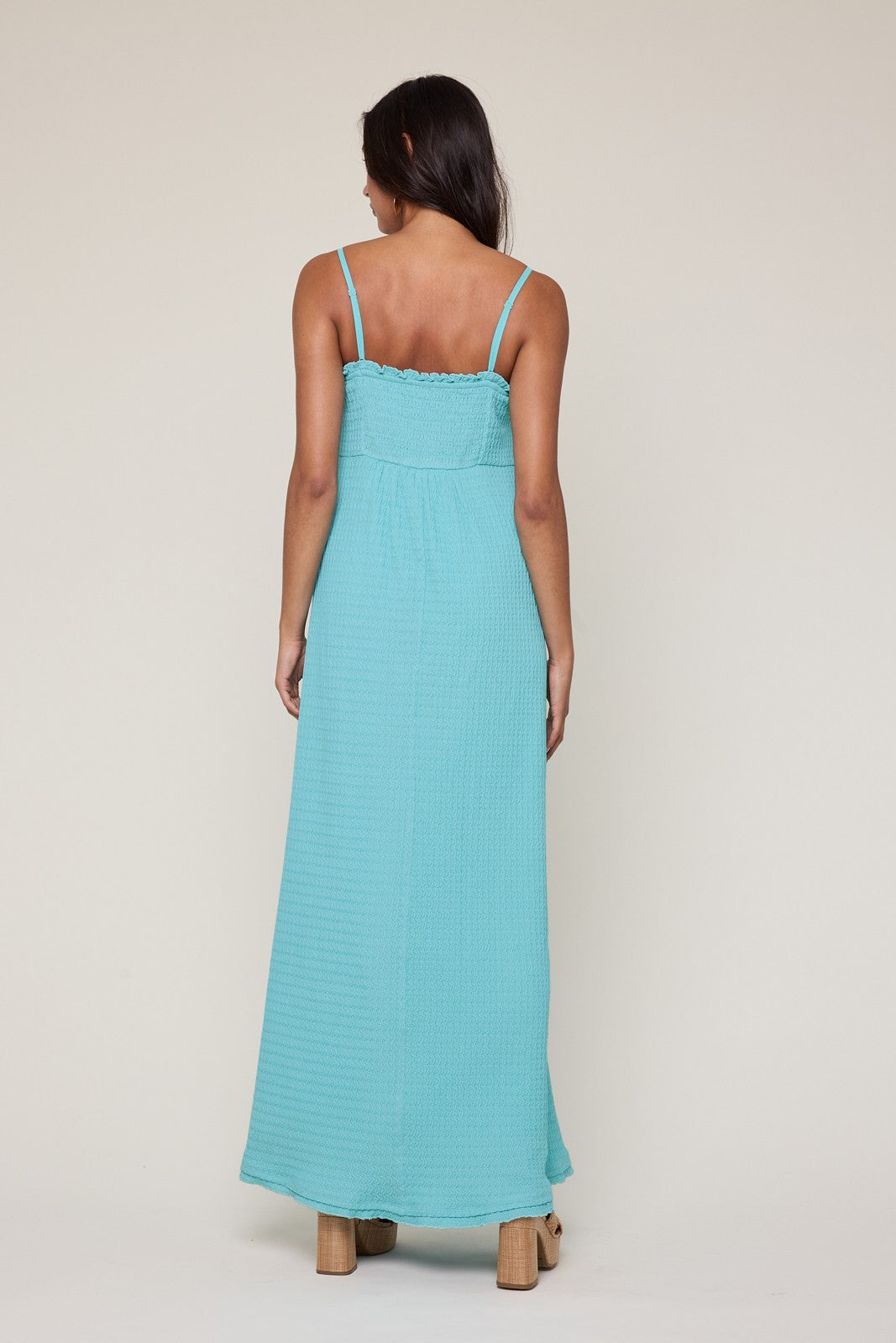 woman wearing a light blue sleeveless maxi dress, shown from the back, with a fitted bodice and flowy skirt