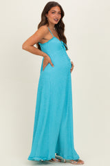 woman wearing a turquoise maternity maxi dress with adjustable straps and a flowing silhouette, showing her baby bump