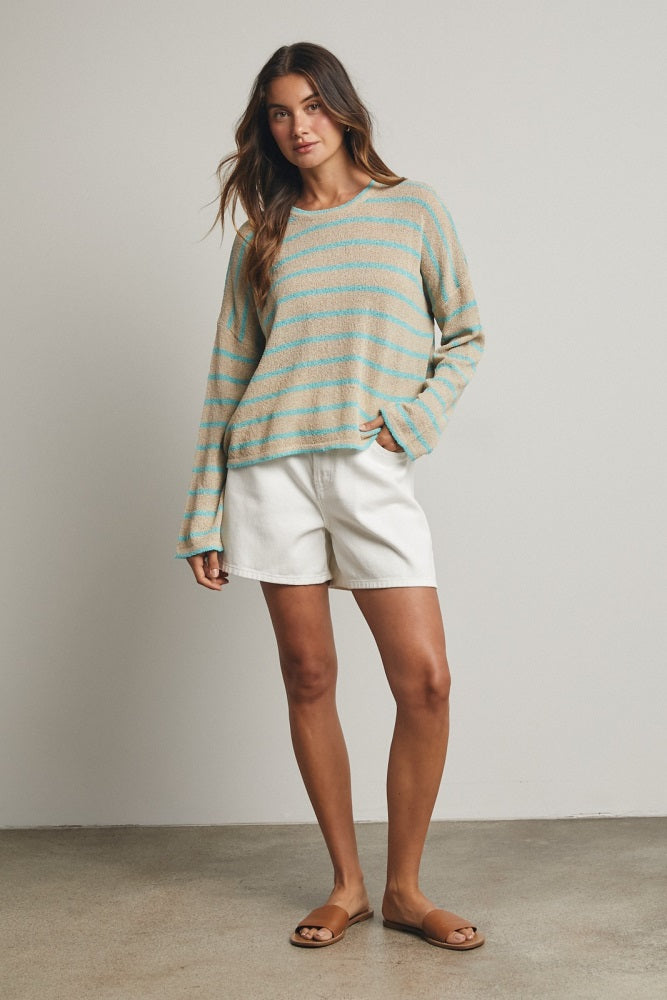 woman wearing a striped long sleeve sweater in turquoise and beige with white shorts and sandals