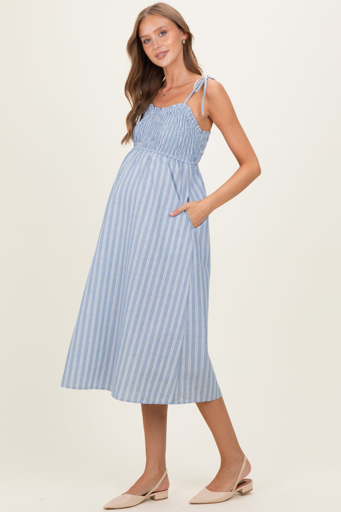 woman wearing a light blue striped maternity dress with adjustable straps and side pockets, showing her baby bump
