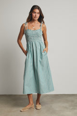 woman wearing a teal and white striped midi dress with smocked bodice and adjustable straps, standing with pockets