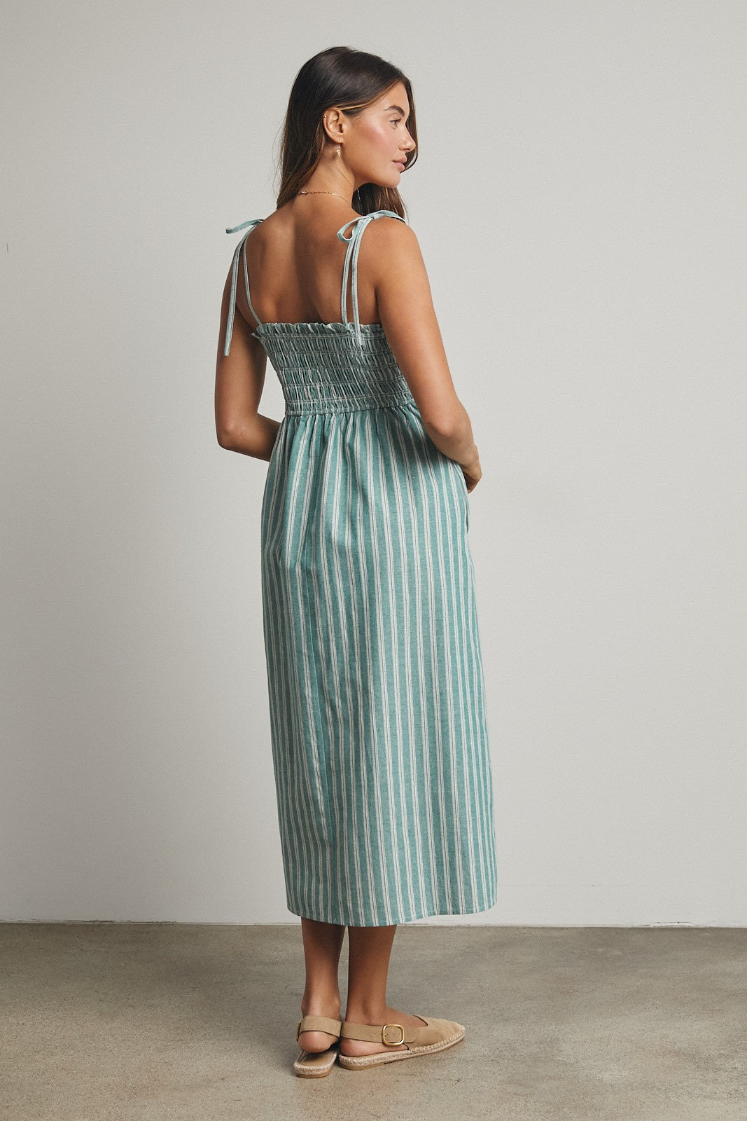 woman wearing a teal and white striped smocked midi dress with adjustable straps and a relaxed fit, viewed from the back