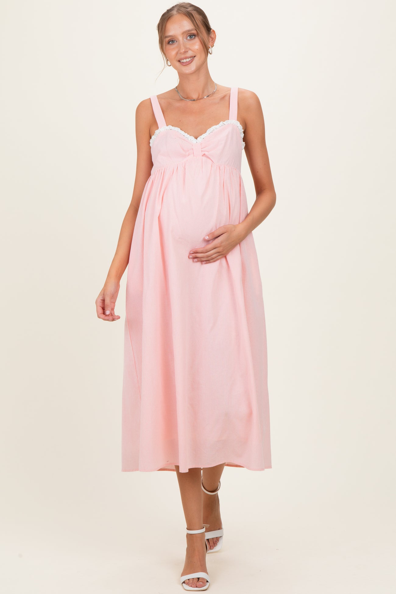woman wearing a pink maternity dress with lace detailing, holding her baby bump, and walking gracefully