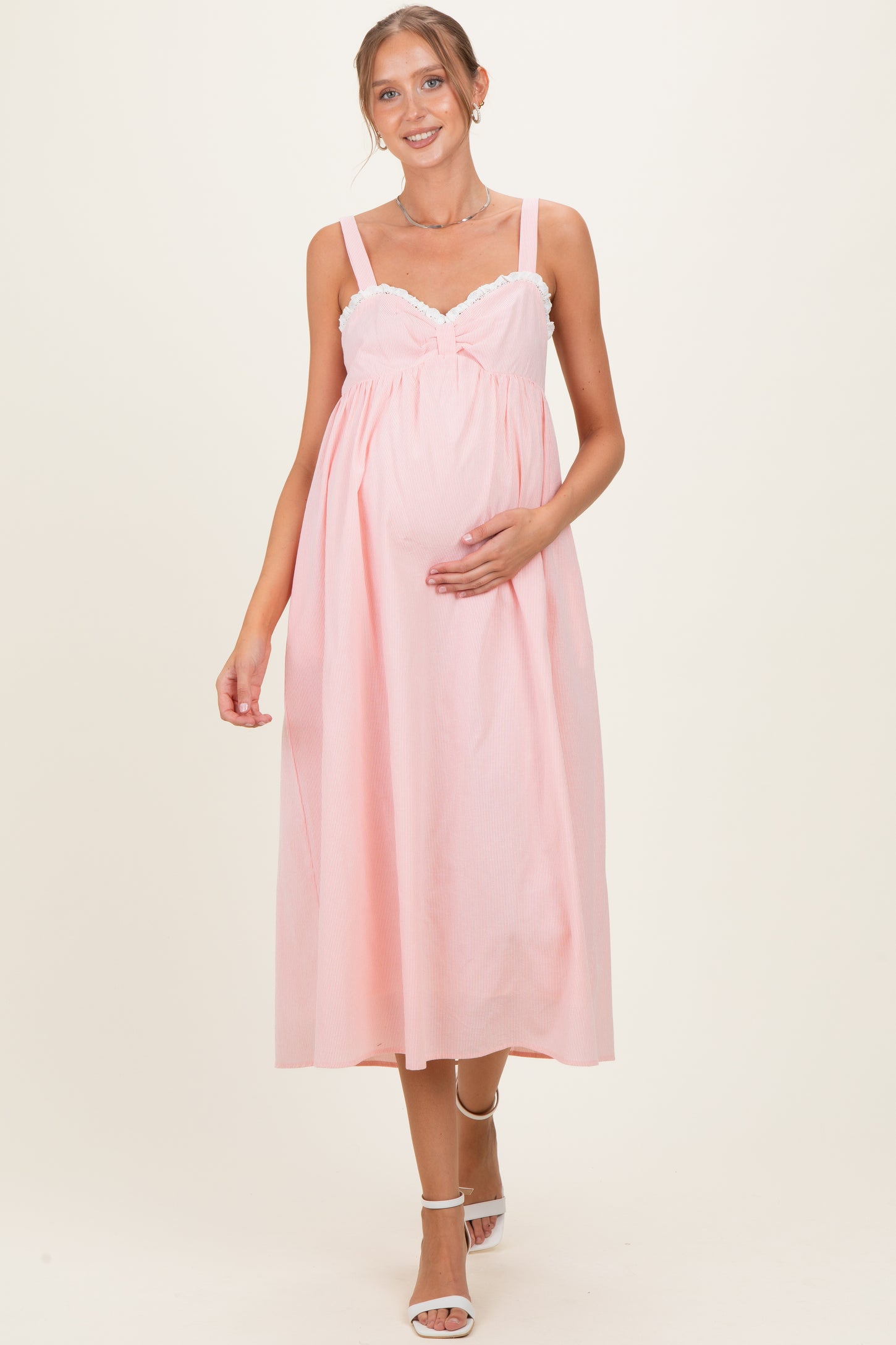 woman wearing a pink maternity dress with lace detailing, holding her baby bump, and walking gracefully
