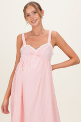 woman wearing a pink striped maternity dress with lace trim and adjustable straps, showing her baby bump