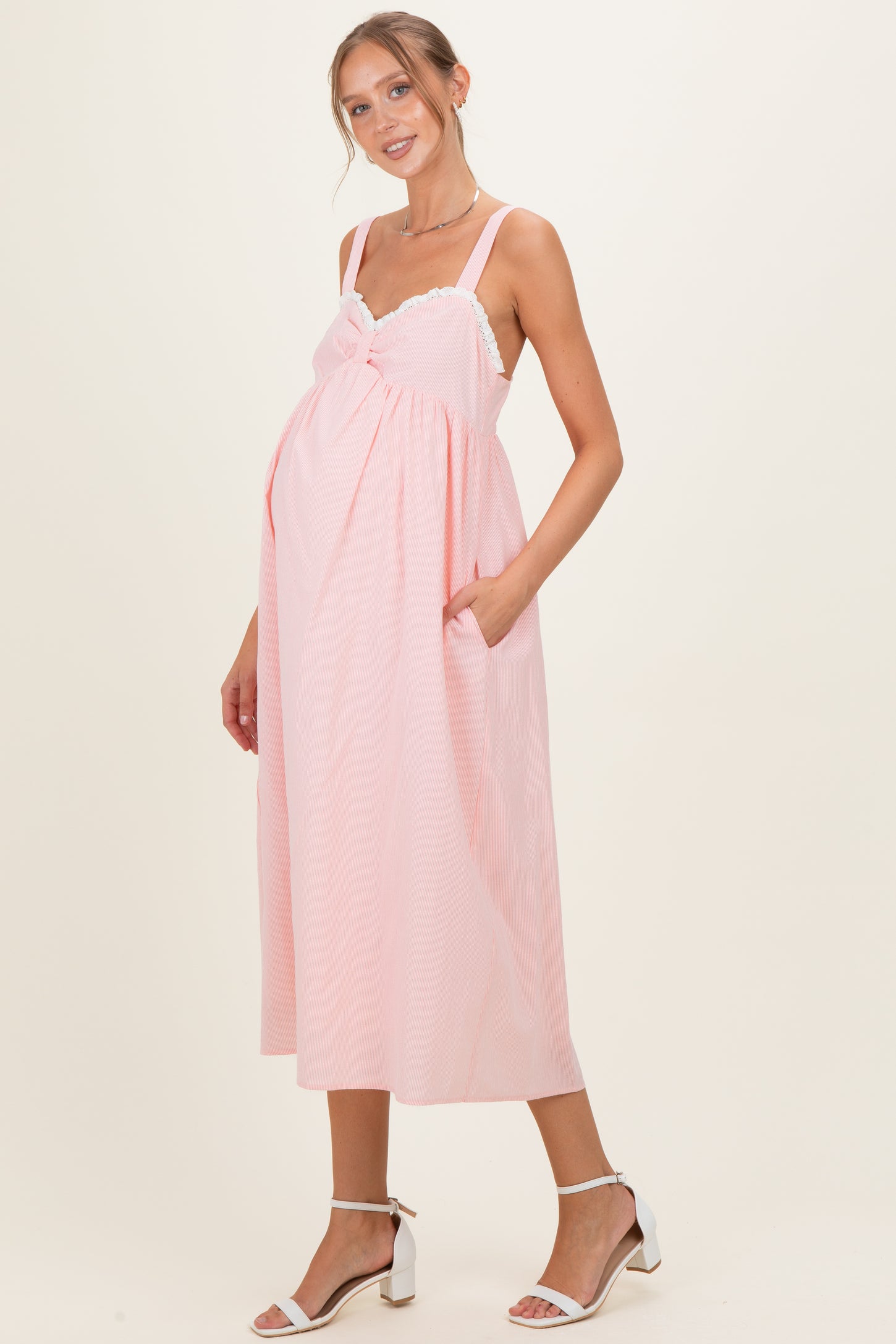 woman wearing a pink maternity dress with a knot detail and pockets, showcasing her baby bump