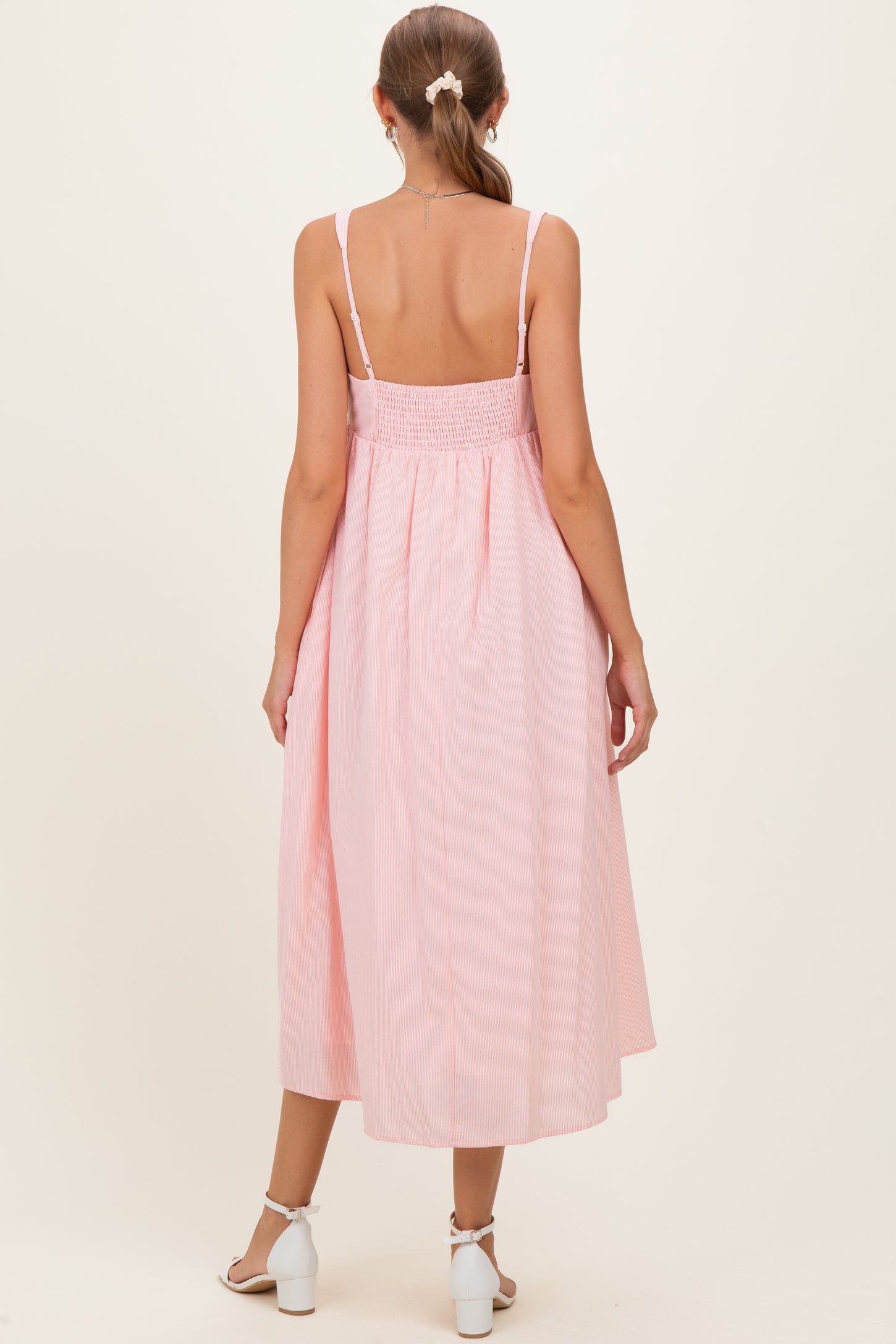woman wearing a light pink striped maternity dress with smocked back and midi length, showing a relaxed fit from the back