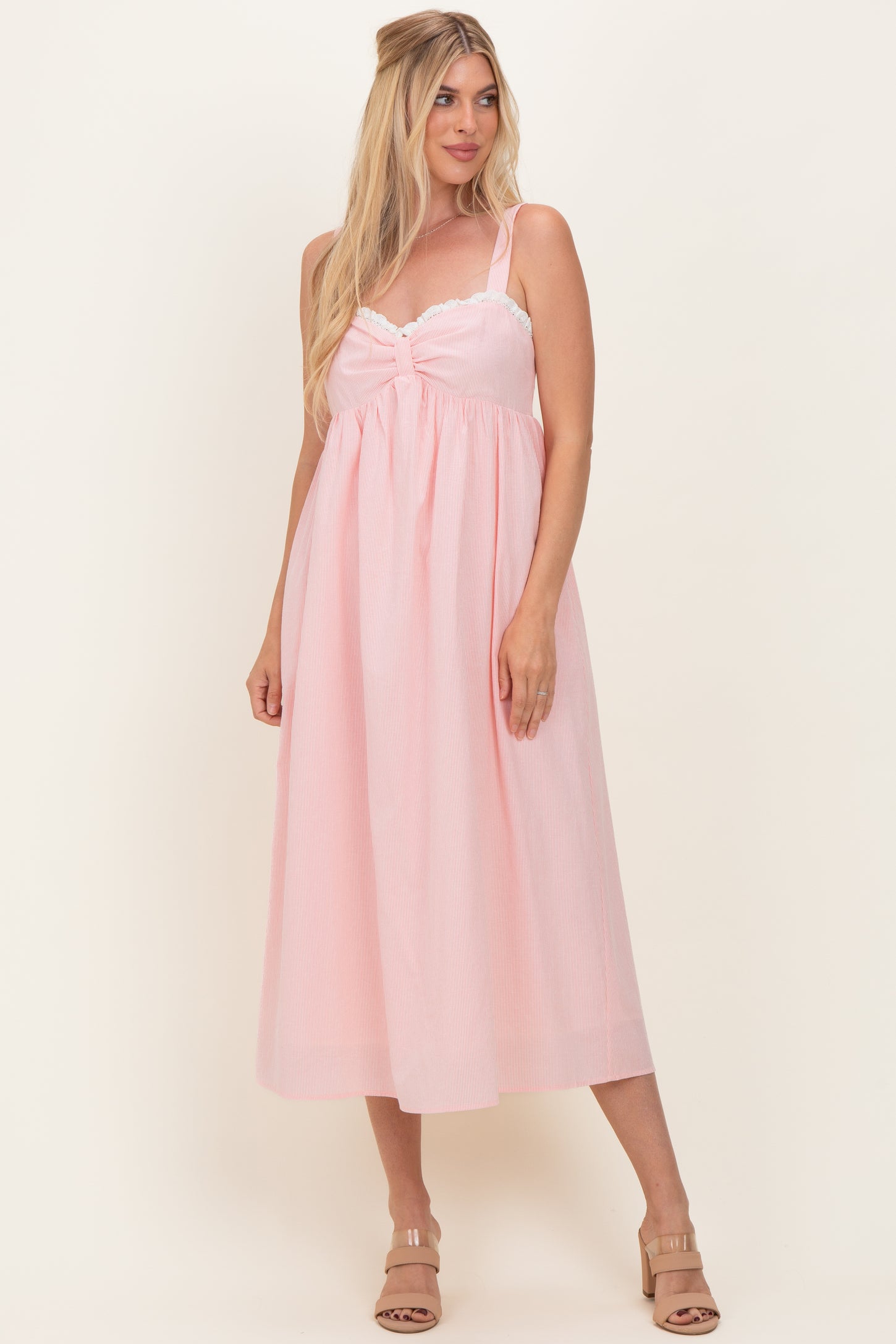 woman wearing a pink midi dress with lace trim and adjustable straps, standing on a neutral background