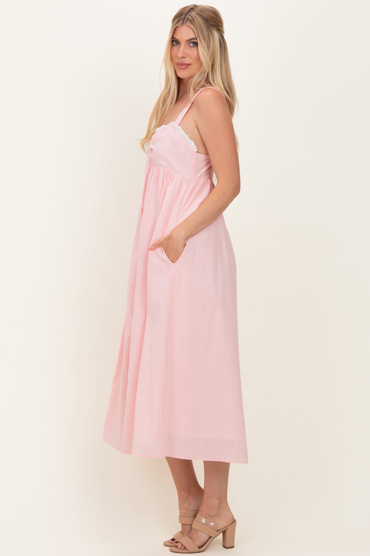 woman wearing a pink striped midi dress with adjustable straps and pockets, styled with strappy sandals