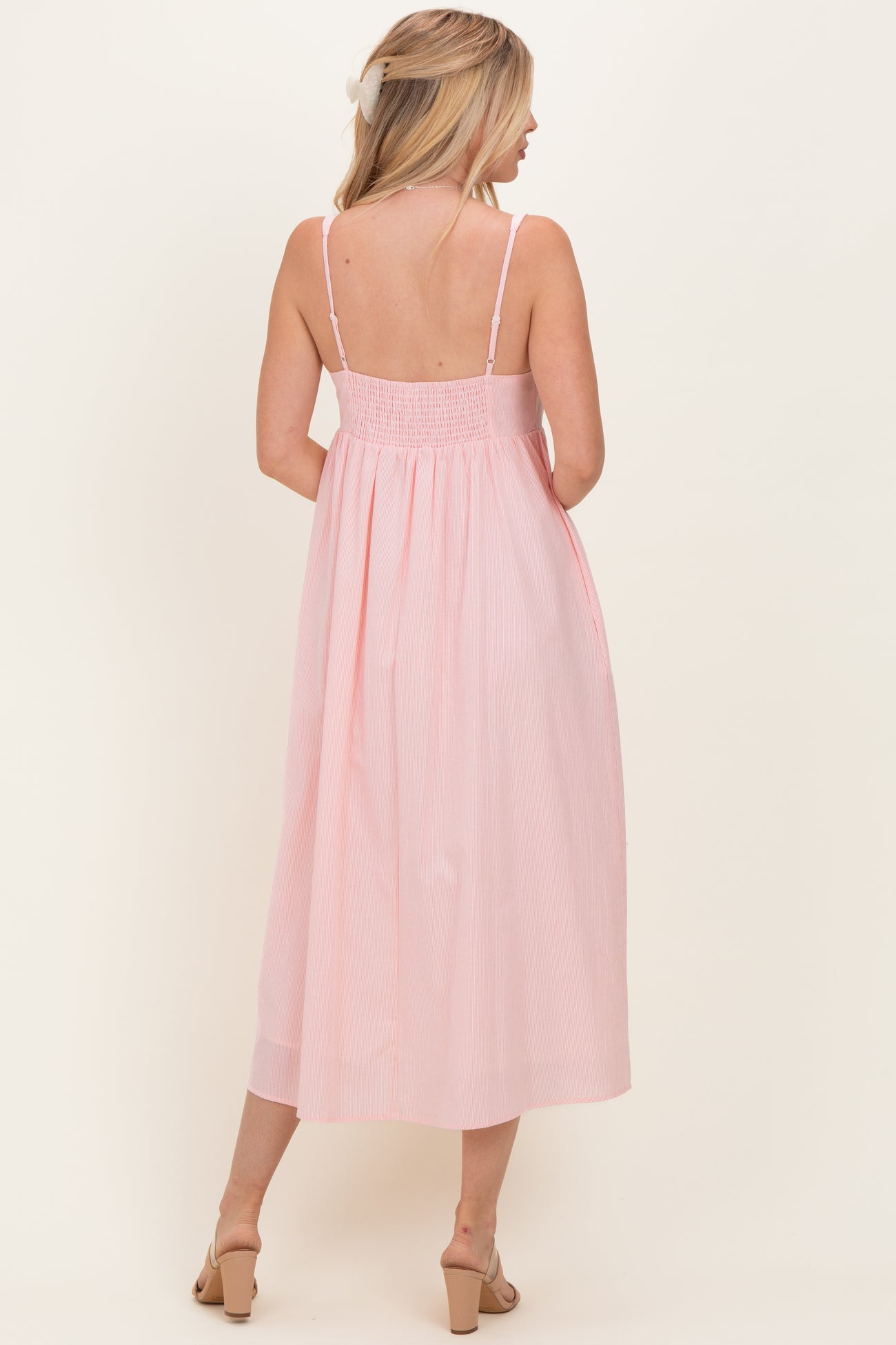 woman wearing a backless pink striped midi dress with thin straps and a smocked bodice