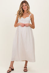 woman wearing a light beige maternity maxi dress with adjustable straps and a ruffled bodice, showing a baby bump