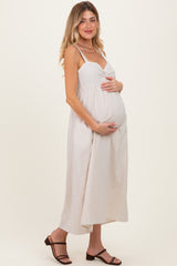 woman wearing a cream maternity maxi dress with a ruffled neckline and holding her baby bump