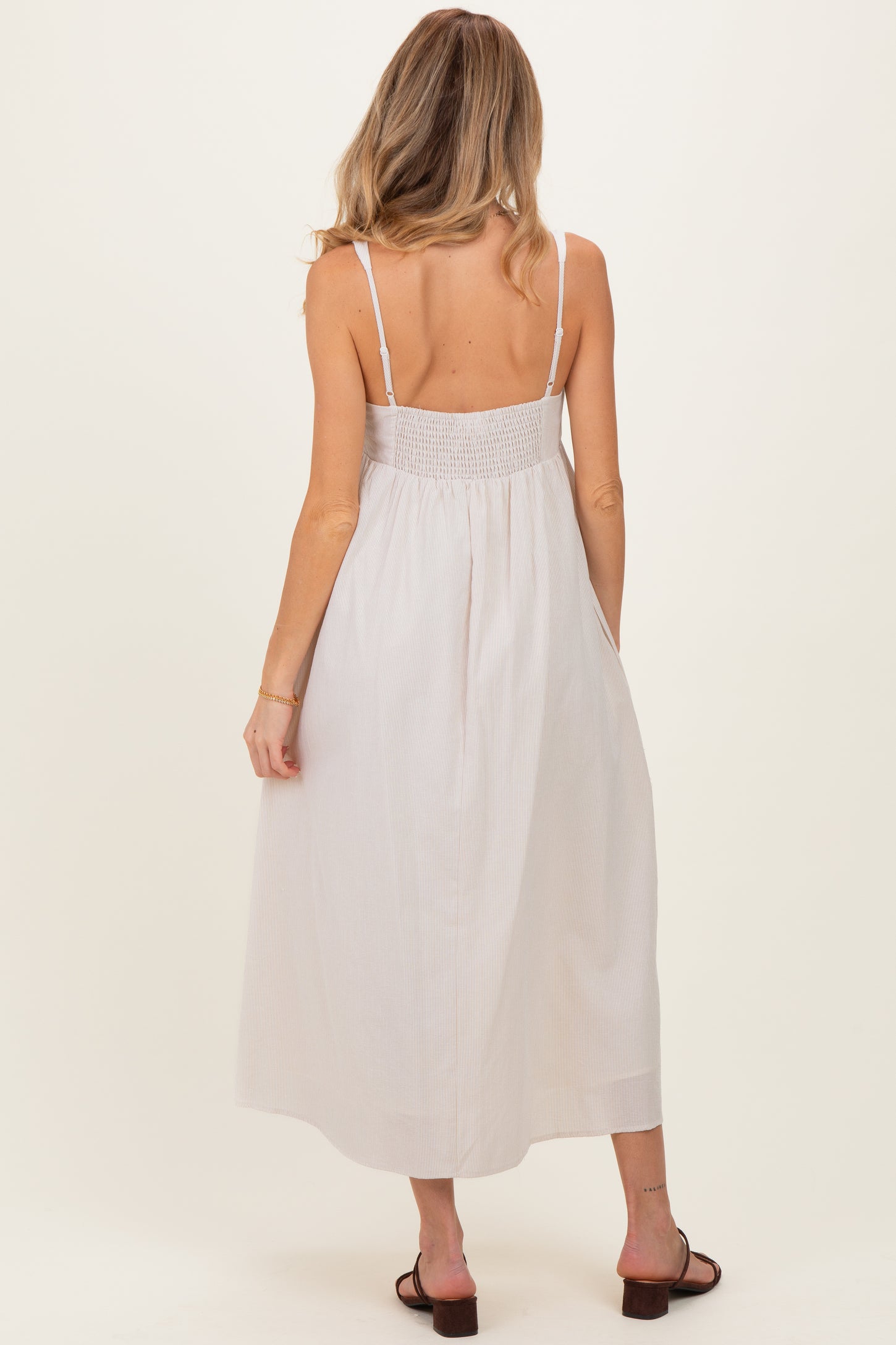 woman wearing a white striped maternity maxi dress with a smocked back and adjustable straps