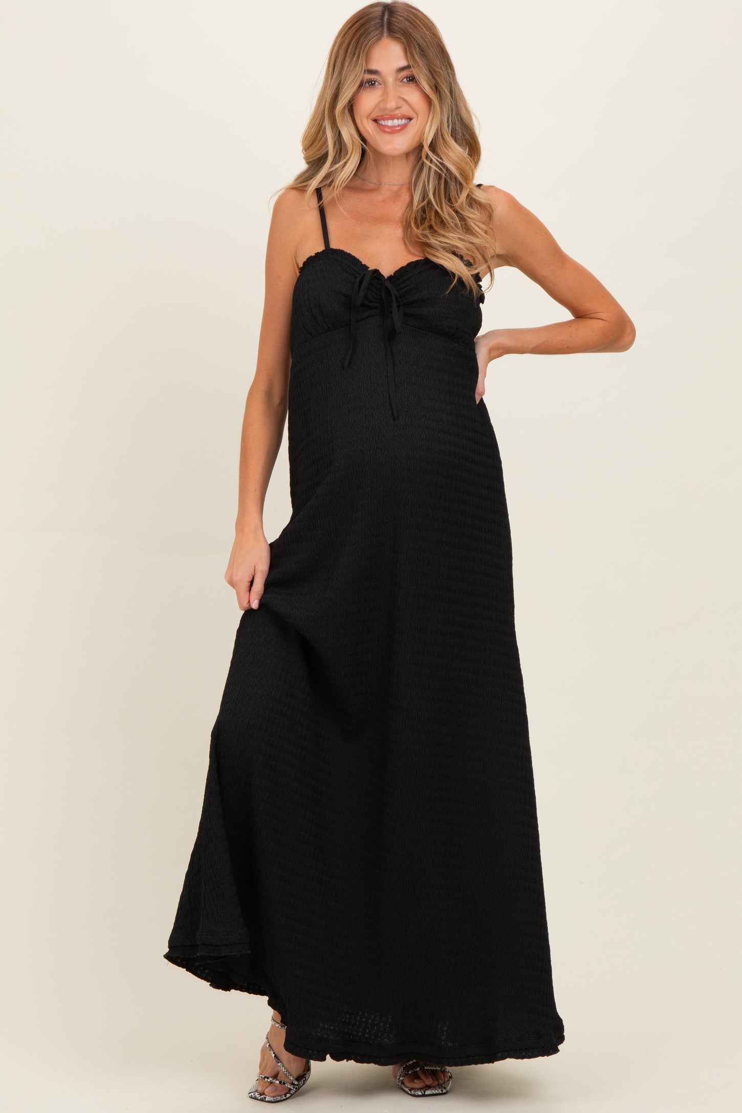 woman wearing a black maternity maxi dress with a tie detail at the bust and a side slit, showing off her baby bump