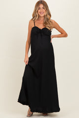 woman wearing a black maternity maxi dress with a tie detail at the bust and a side slit, showing off her baby bump