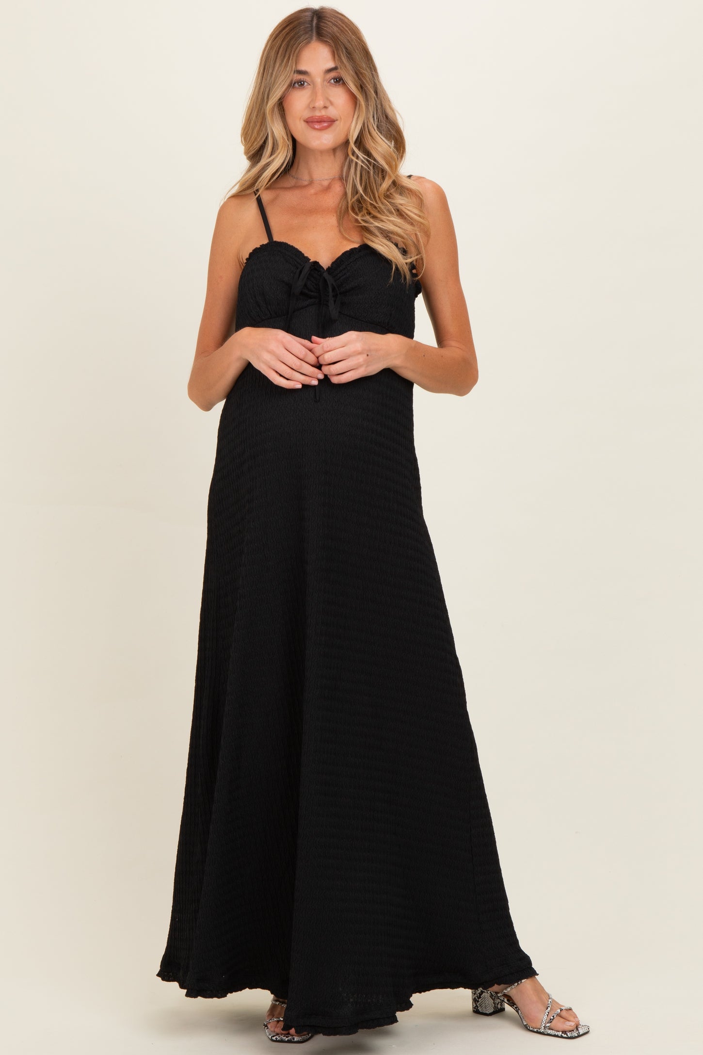 woman wearing a black maternity maxi dress with a tie front and spaghetti straps, showcasing her baby bump