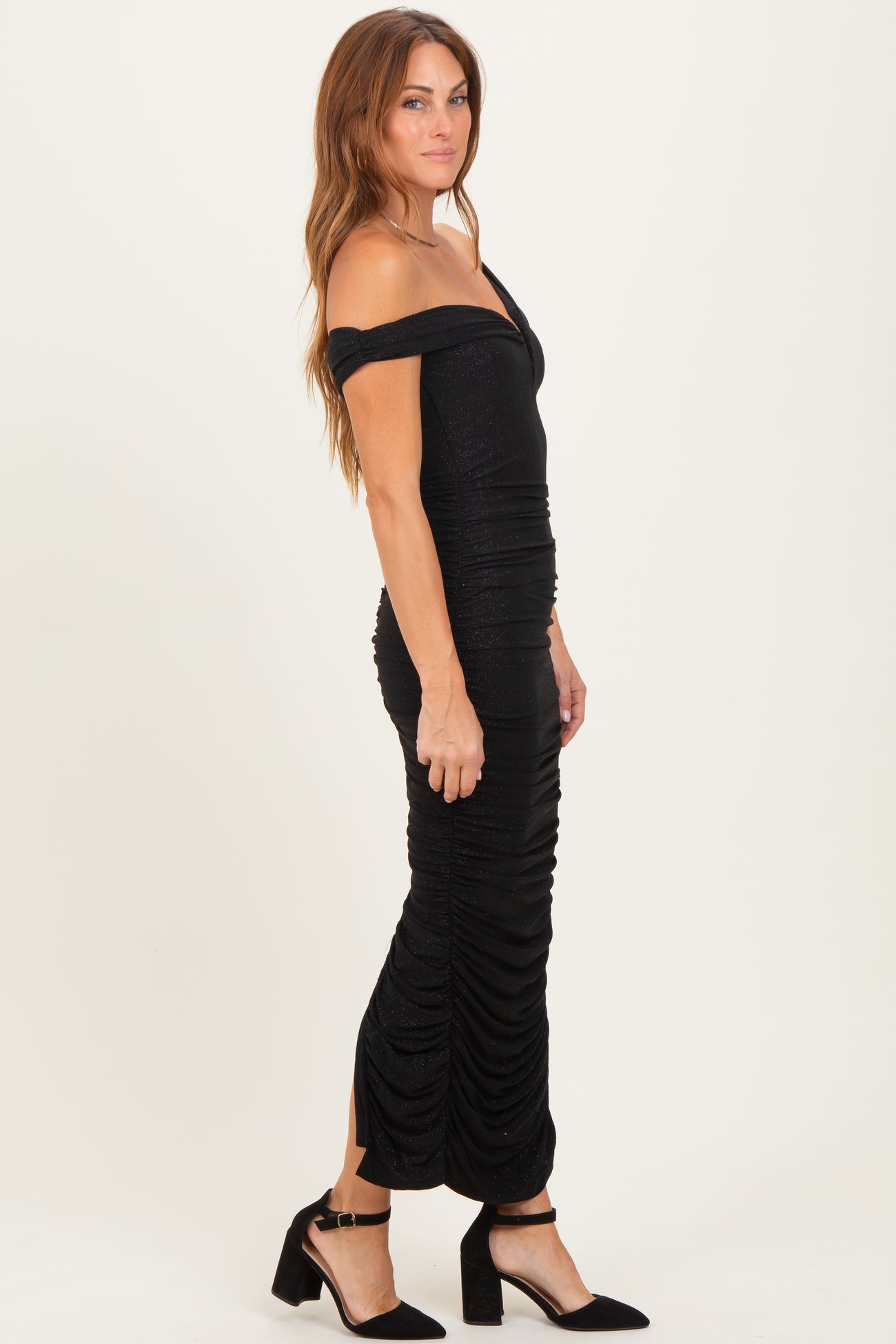 woman wearing a black off-shoulder ruched midi dress with a fitted silhouette and strappy heels
