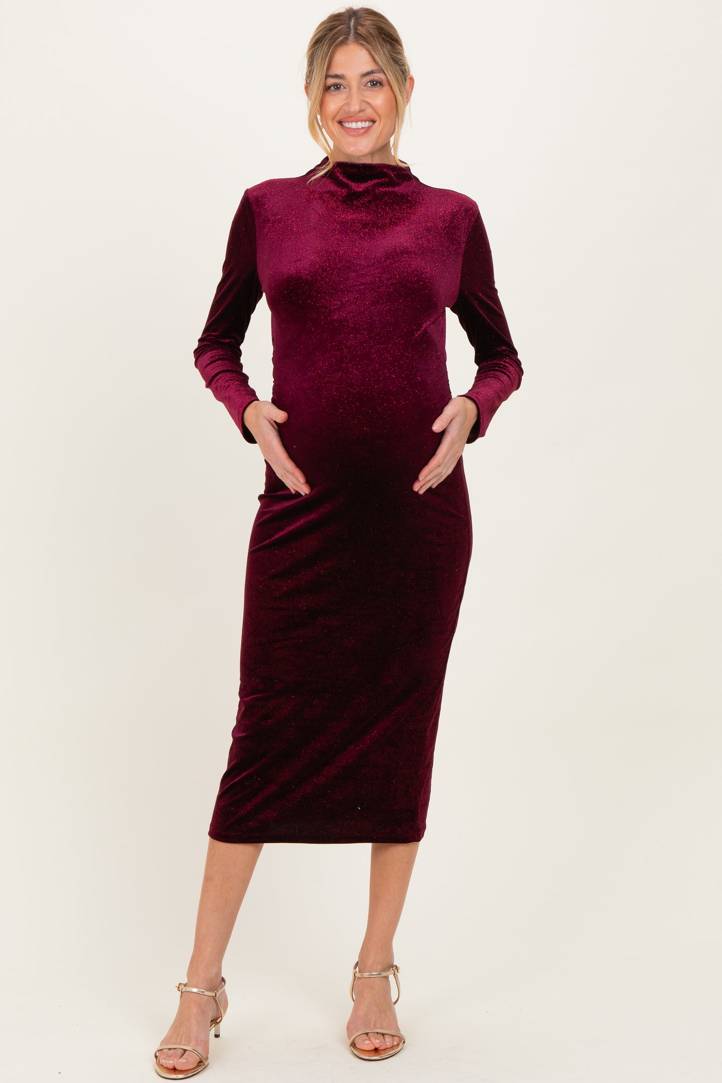 woman wearing a burgundy velvet long sleeve maternity dress and cradling her baby bump