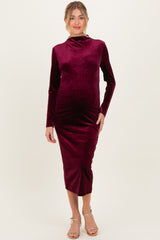 woman wearing a burgundy long sleeve maternity dress with a fitted silhouette and high neckline, showing her baby bump
