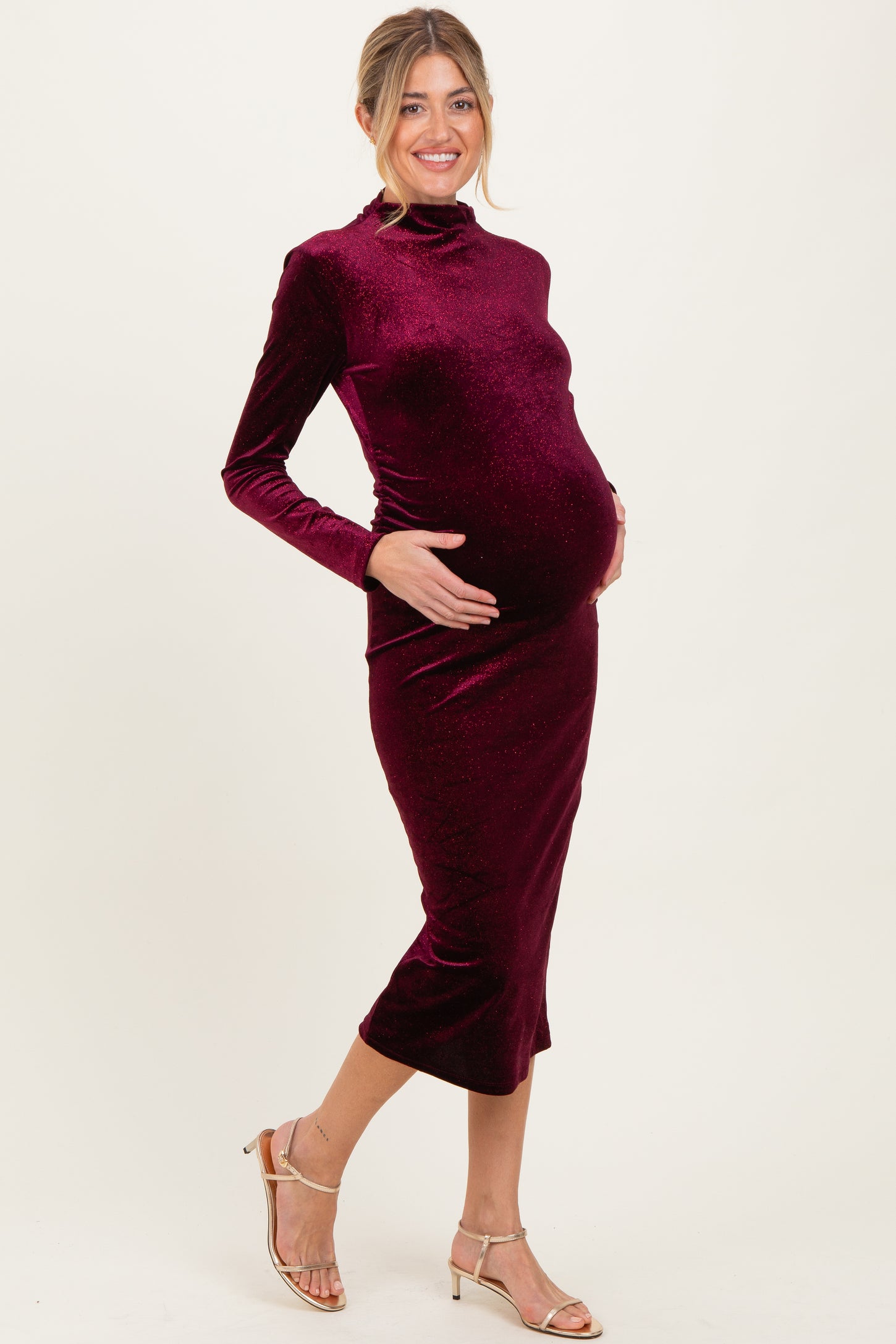 woman wearing a burgundy velvet long sleeve midi dress showcasing her baby bump