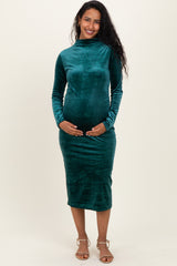 woman wearing a green velvet long sleeve maternity dress and holding her baby bump