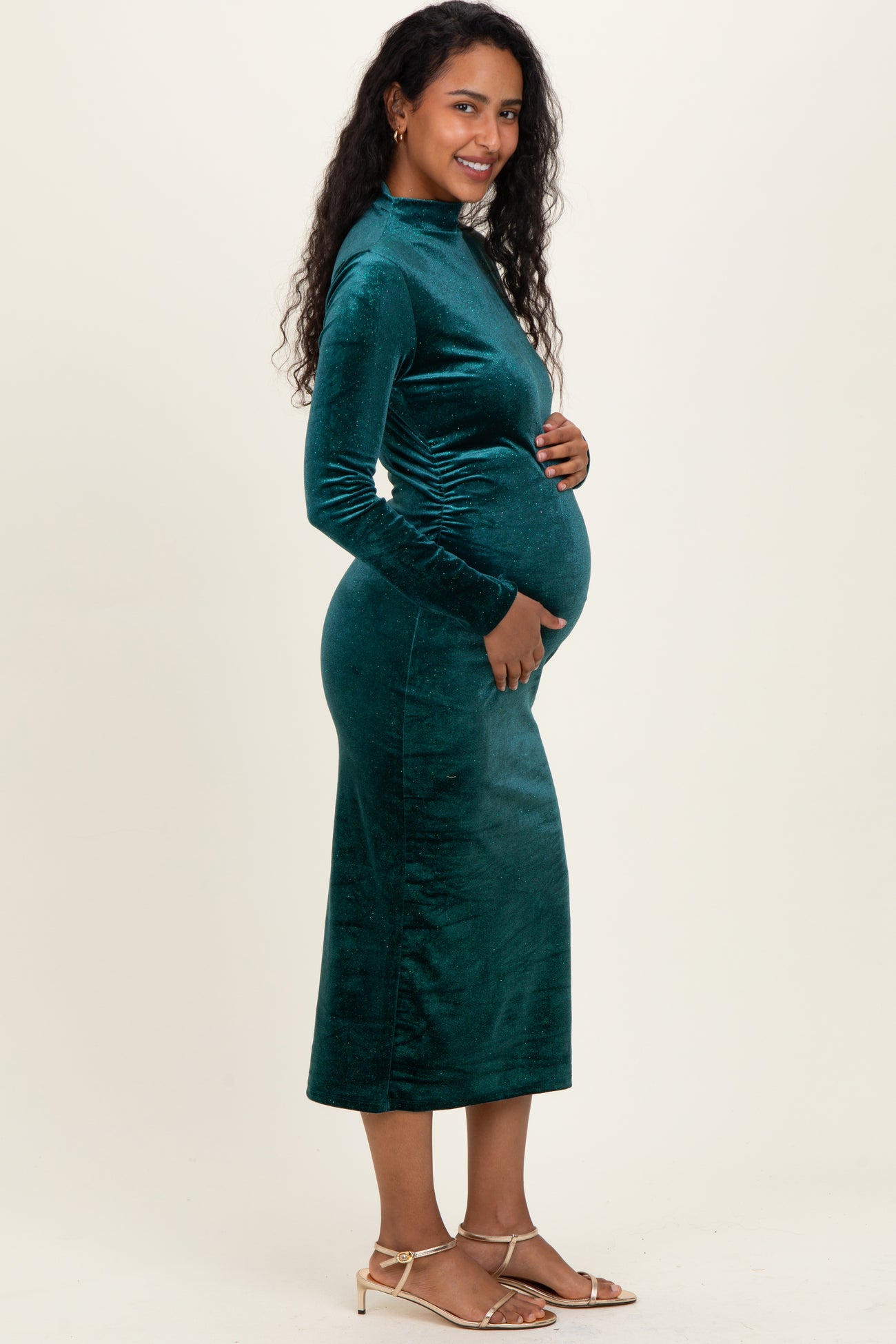 woman wearing a green velvet long sleeve maternity dress and holding her baby bump