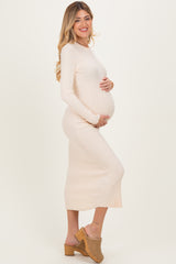 woman wearing a light pink ribbed maternity dress, holding her baby bump while smiling