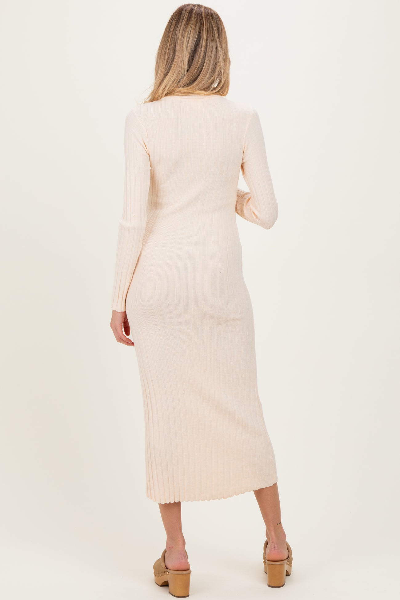 woman wearing a light peach long sleeve ribbed maternity dress, showing a fitted silhouette and midi length