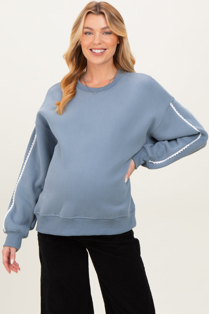 woman wearing a blue maternity sweatshirt with white trim details, showing her baby bump and smiling