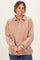 woman wearing a beige oversized pullover with a polo collar and button detail, smiling against a plain background
