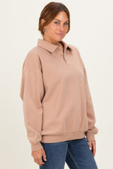 woman wearing a beige oversized polo sweatshirt with a collared neckline and button-up detail, paired with blue jeans