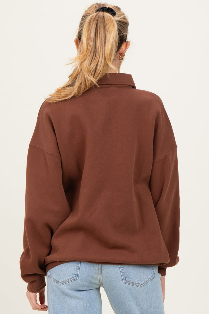 woman wearing a brown oversized maternity sweatshirt, view from the back, with light blue jeans.