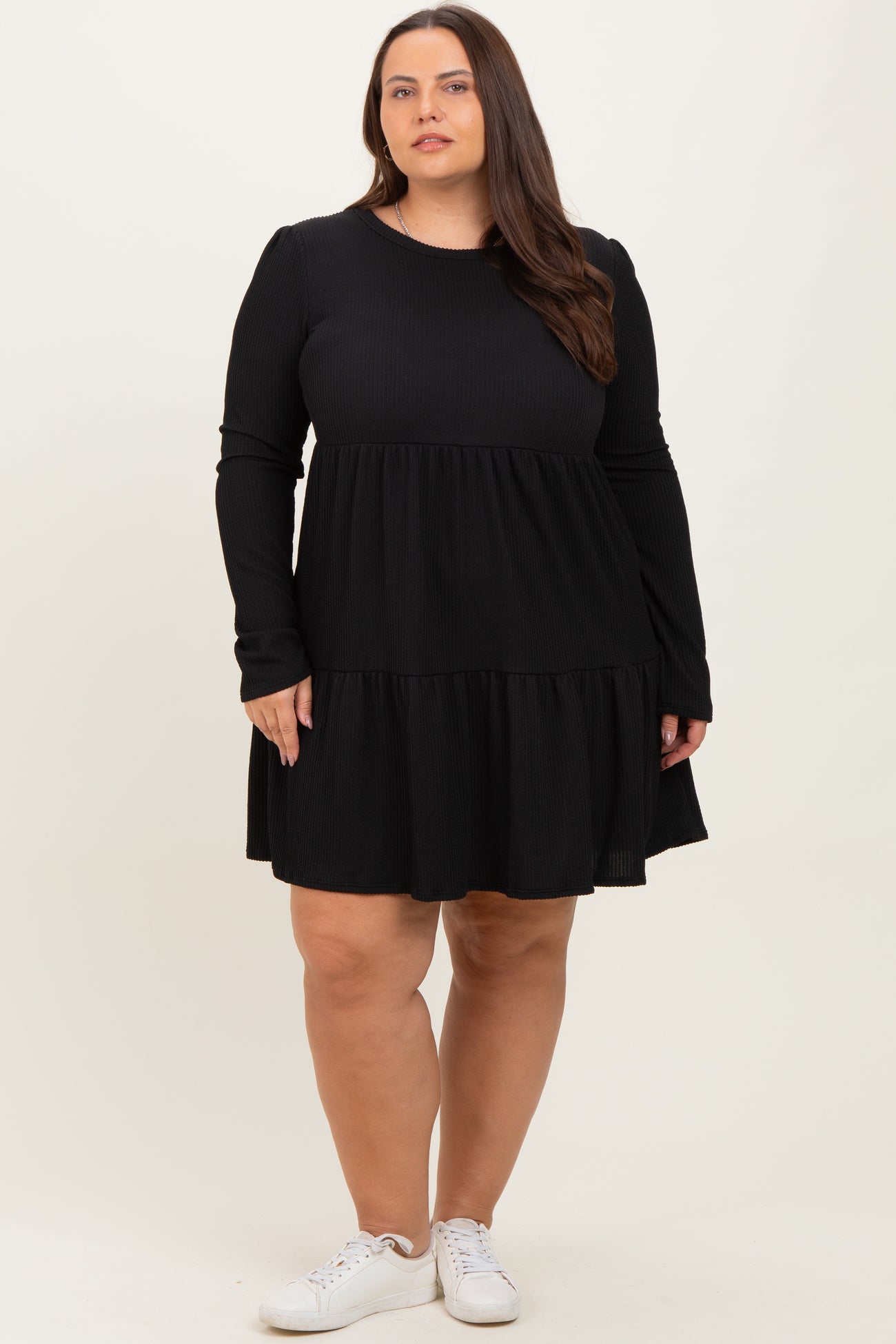 woman wearing a black long sleeve plus size dress with a tiered skirt and white sneakers