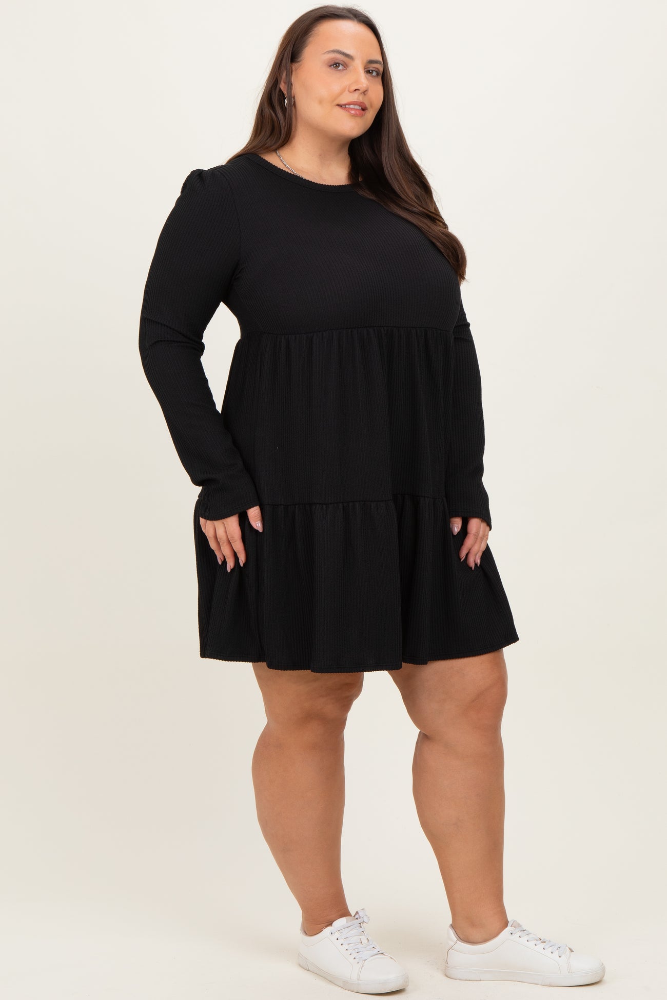 woman wearing a black long sleeve tiered dress with a ribbed texture and white sneakers