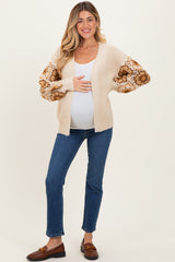 woman wearing a beige maternity cardigan with floral sleeves and a visible baby bump, paired with blue jeans