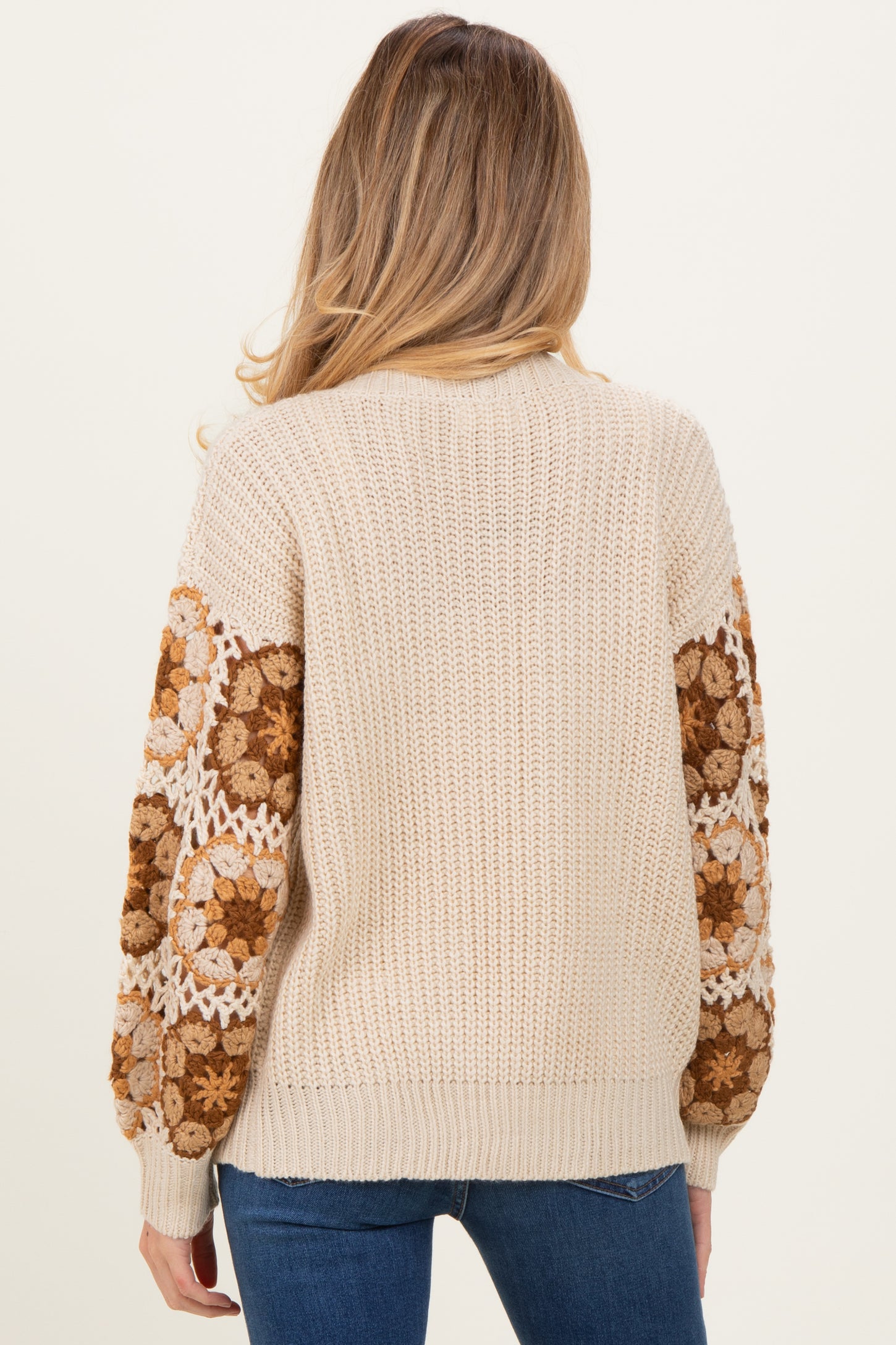 woman wearing a beige knit maternity sweater with floral-patterned sleeves and a relaxed fit, showcasing her baby bump