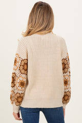 woman wearing a beige knit maternity sweater with floral-patterned sleeves and a relaxed fit, showcasing her baby bump