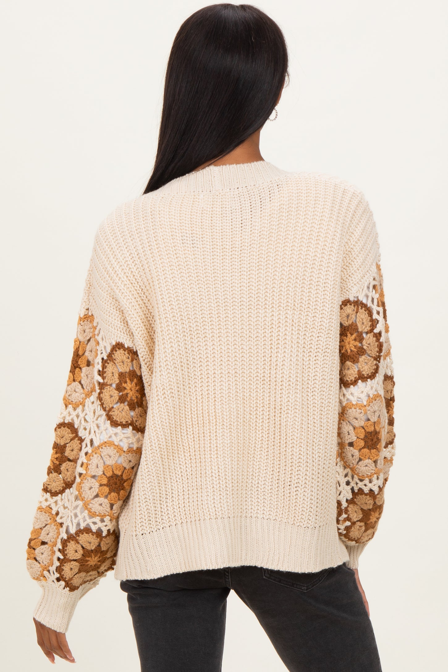 woman wearing a cream-colored knit sweater with floral patterned sleeves and a relaxed fit