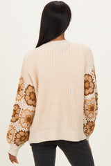 woman wearing a cream-colored knit sweater with floral patterned sleeves and a relaxed fit