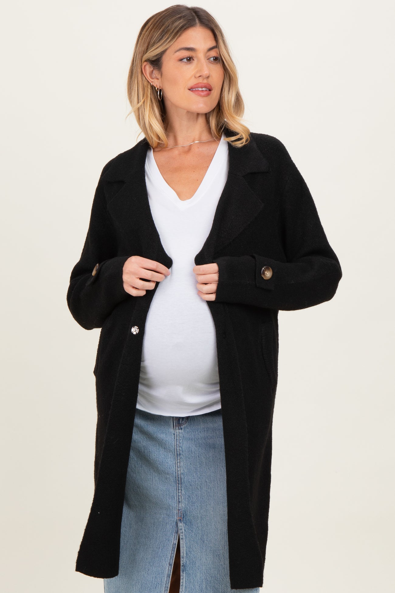 woman wearing a black maternity cardigan over a white top and showing her baby bump, styled with a denim skirt