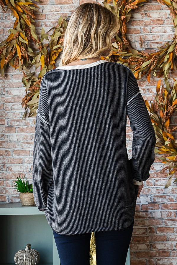 woman wearing a black and white striped oversized sweater, facing away, styled with blue jeans and set against a brick wall backdrop