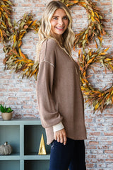 woman wearing a brown oversized textured sweater with long sleeves, standing against a brick wall with autumn decor