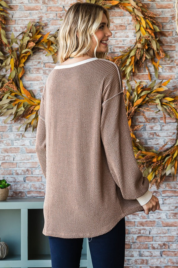 woman wearing a brown waffle knit sweater with a white trim and relaxed fit, shown from the back against a rustic background