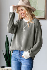 woman wearing a green ribbed oversized sweater with white cuffs and smiling, paired with blue jeans