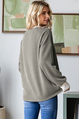woman wearing a loose-fitting olive green ribbed sweater with long sleeves and contrasting cream cuffs, seen from the back